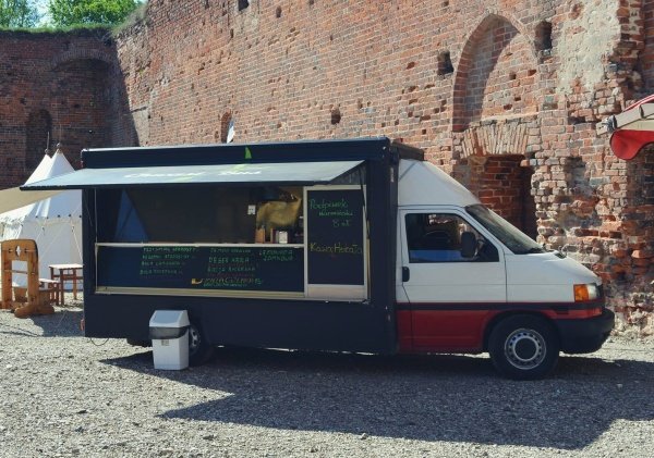 Zdjęcie przedstawia food tracka na tle zamku Dybowskiego