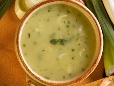 Zdjęcie przedstawia miseczkę z kremem z pora, dookoła miseczki leżą kawałki pora i bagietka