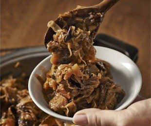 Na zdjęciu ręka trzymająca miseczkę z porcją bigosu szałwiowego