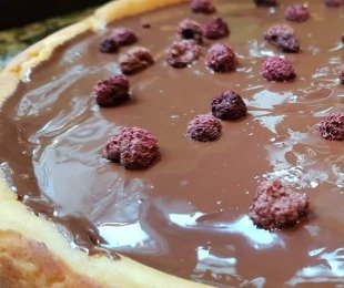 Na zdjęciu sernik piernikowo waniliowy z tofu polany czekoladą, udekorowany malinami