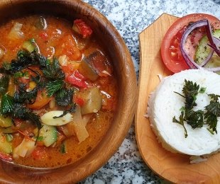 Na zdjęciu drewniana miska, wypełniona potrawą - Ratatouille z Pokrzywami, obok drewniany talerzyk z ryżem i warzywami