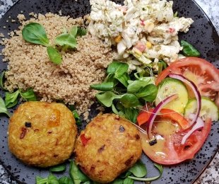 Na zdjęciu talerz, na nim Kotlety z brązowego ryżu z curry podane z kaszą, surówkami, warzywami i sosami