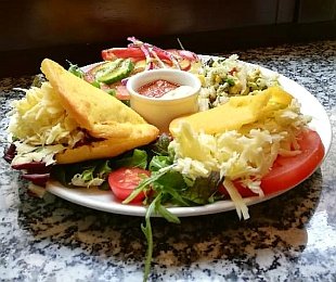 Na zdjęciu talerz, na nim potrawa Arepas podana z surówką, warzywami i sosami