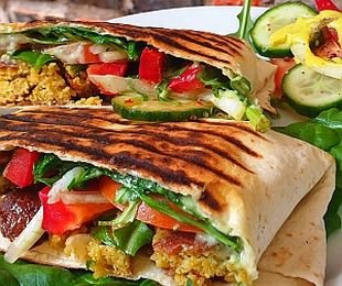 Zdjęcie przedstawia potrawę falafel z warzywami i sosami zapieczoną w tortilli