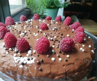 Zdjęcie przedstawia ciasto bananowe polane czekoladą przyozdobione malinami