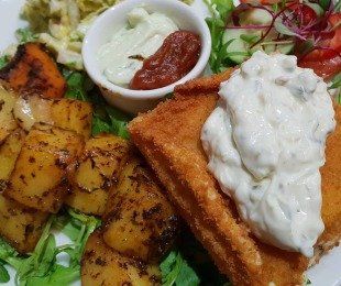 Zdjęcie przedstawia potrawę smażony ser z sosem tatarskim, pieczonymi ziemniakami i surówką